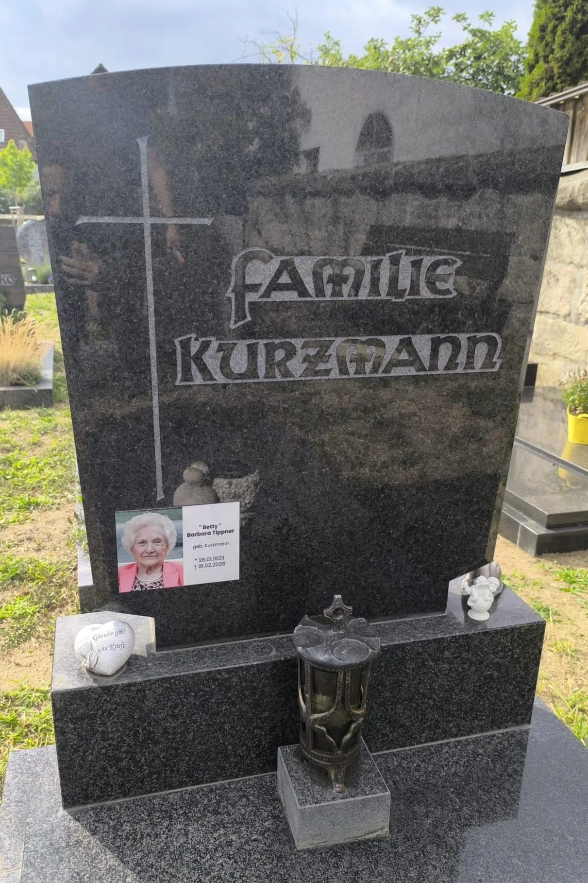 Rechteckige Aluminiumplatte mit Foto und der Aufschrift Betty Barbara Tippner an einem Grabstein der Familie Kurzmann